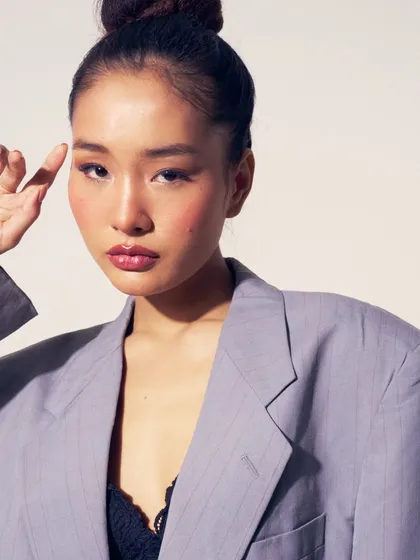 A soft glam look with a focus on glowing skin and a subtle, rosy flush. The hair is styled in a chic top-knot, and the oversized blazer adds a touch of effortless cool.