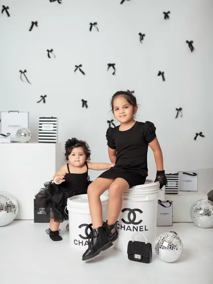 A full view of the sisters posing in their chic black outfits. The custom props and background really bring this creative theme to life.