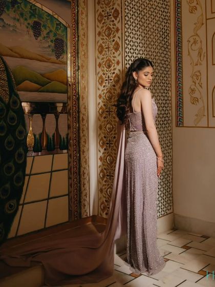 An elegant bridal portrait showcasing the beautiful drape and trail of her lavender gown against an ornate, artistic wall.