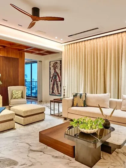 This living room perfectly captures the essence of living in a place like Mumbai, filled with serenity and elegance. The combination of rich wood paneling, a coffered ceiling, and luxurious marble flooring creates a timeless and sophisticated look.