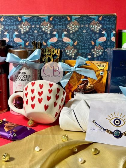 A luxurious Rakshabandhan hamper for your sibling. This beautiful peacock-themed box is filled with a heart-printed mug, a shirt, Pringles, cookies, chocolates, and an evil eye rakhi.