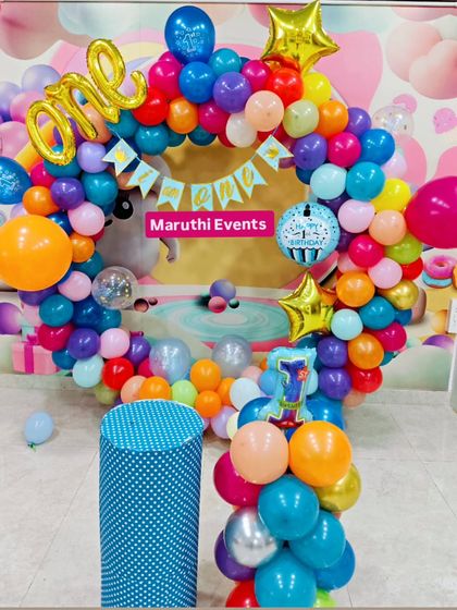 A vibrant rainbow-colored circular balloon arch for a first birthday. The "ONE" foil balloon and number "1" candle add the perfect finishing touches.