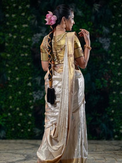 An elegant look for a festival. The focus is on the beautiful off-white and gold saree, complemented by a traditional braid with a fresh pink lotus.