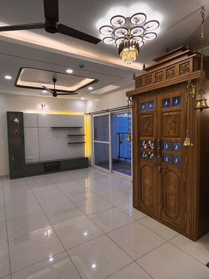 A picture-perfect view of a recently completed project. This living room features a contemporary TV unit that contrasts beautifully with a traditional, intricately carved wooden pooja unit, showing how we can blend different styles.