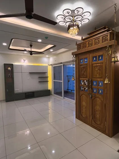 A picture-perfect view of a recently completed project. This living room features a contemporary TV unit that contrasts beautifully with a traditional, intricately carved wooden pooja unit, showing how we can blend different styles.