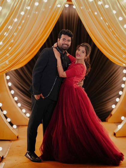 A glamorous couple poses against a stage-like backdrop with dramatic yellow curtains and lights.