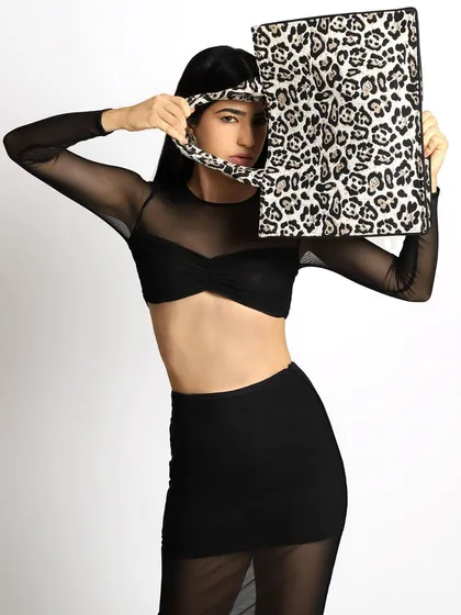 This shot features a model in a sheer black outfit, using a leopard-print tote bag to partially obscure her face. The playful yet chic pose highlights the accessory while maintaining a high-fashion, editorial feel.
