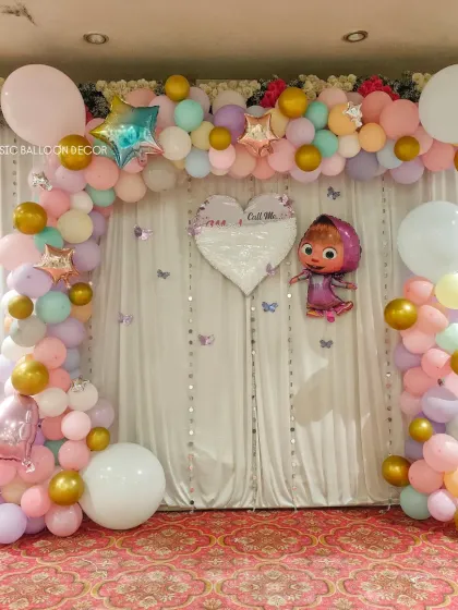 This naming ceremony backdrop features a Masha and the Bear theme. A pastel balloon arch frames a white curtain backdrop with a custom heart-shaped sign.