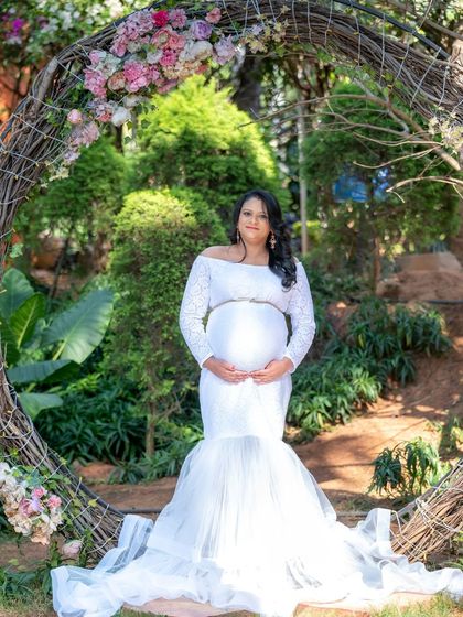 An angelic portrait of a mom-to-be in a white lace gown. She stands inside a rustic floral wreath, creating a soft and romantic outdoor scene.