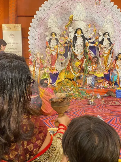 An over the shoulder view showing a devotee's perspective during the Dhunuchi Naach, with the magnificent Durga idol in the background.