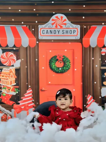 A festive Christmas candy shop theme, with a baby girl in a red velvet dress sitting amidst a snowy, sweet-filled wonderland.