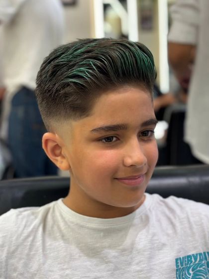 A fun and bold look for a young client, combining a sharp fade haircut with vibrant green highlights on top.