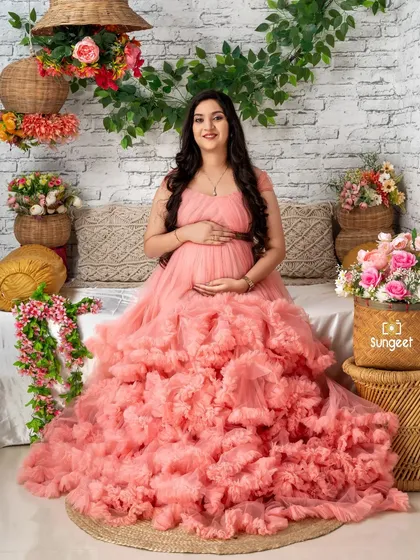 A sweet and serene portrait of a mom-to-be in a pink ruffled gown, seated in our charming floral-themed setup.
