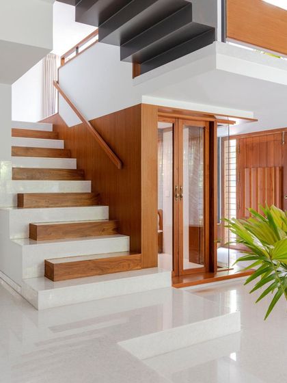 The main staircase in the 'Copper House' combines white marble with solid teak wood treads. This material transition marks the ascent from the public ground floor to the private upper levels, reflecting a shift in the home's spatial character.