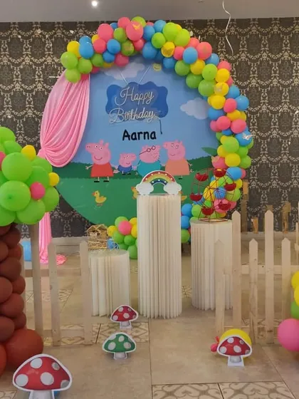 A playful Peppa Pig theme with a circular backdrop showing the whole family. The setup includes a balloon tree and mushroom props to recreate Peppa's world.