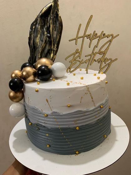 A modern grey and white birthday cake with black and gold accents.