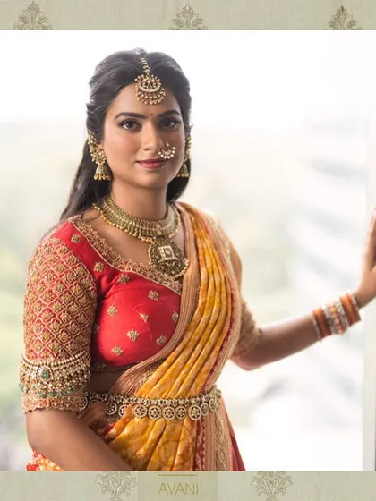 A bride wearing a red and yellow half-saree for her wedding ceremony. The blouse features heavy, traditional embroidery on the sleeves, adding to the richness of her bridal look.