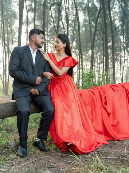 A couple shares a quiet moment during their pre-wedding shoot in a forest, with the bride's long red trail adding a pop of color.