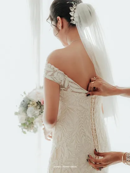 A detail shot showing a hand lacing up the back of the bride's intricate gown, a moment of preparation and anticipation.
