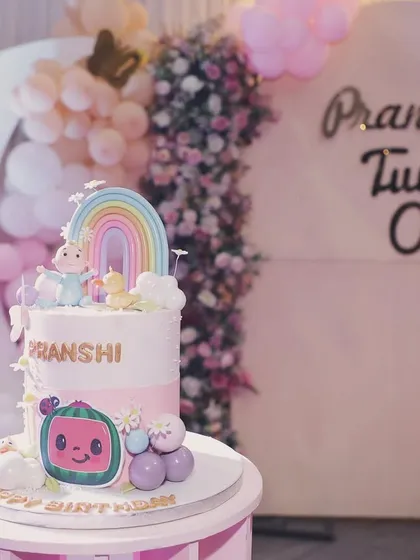 The beautiful Cocomelon and rainbow-themed cake sits perfectly in front of the dreamy, cloud-filled backdrop, tying the whole theme together.