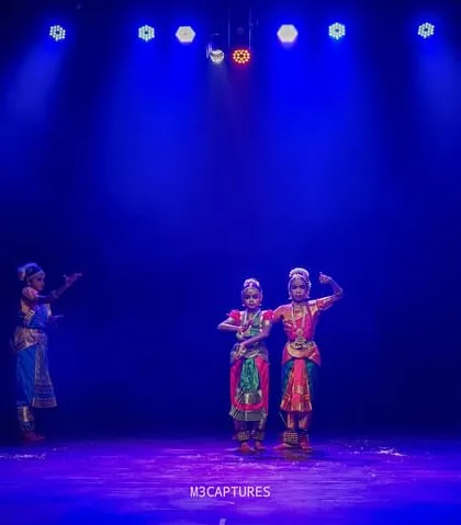 A group of dancers arranged in a creative formation at the 'SADHANA Dance Festival', with two dancers in the center and others surrounding them.