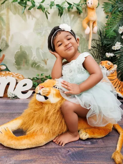 A sweet and sassy pose from a little girl sitting on her lion friend during her jungle-themed birthday shoot.