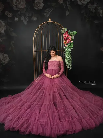 A serene and contemplative pose. Seated by the birdcage, the mom-to-be looks down at her bump, lost in a quiet moment of connection.