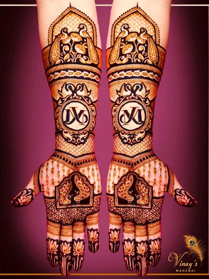 A grand bridal design with personalized initials 'VK' on the arms, surrounded by peacocks and traditional architecture.