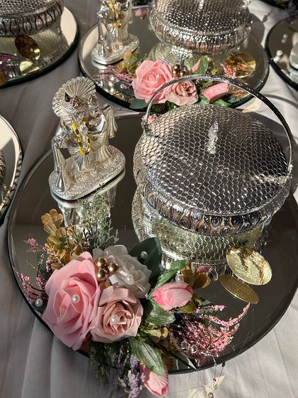 This silver-themed wedding favour is perfect for adding a touch of royalty. It features a mirrored tray with a silver-plated dry fruit box and a Ganesha idol, decorated with pink flowers for a soft, elegant look.