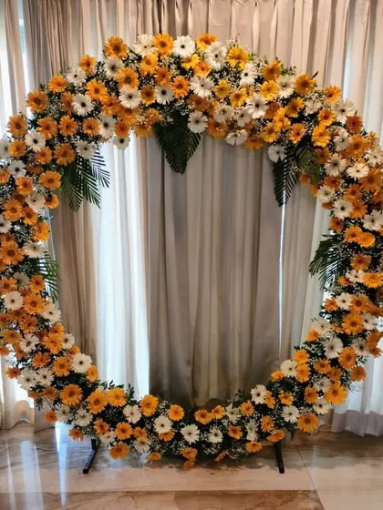This circular floral arch, made with a mix of orange and white gerbera daisies, is a versatile piece. It serves as a modern backdrop for home events, from Ganpati celebrations to engagement parties.