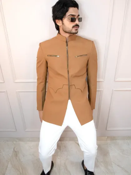 A modern tan bandhgala jacket with a full front zipper and functional zip pockets. Paired with white trousers, this creates a sharp, contemporary look for any celebration.