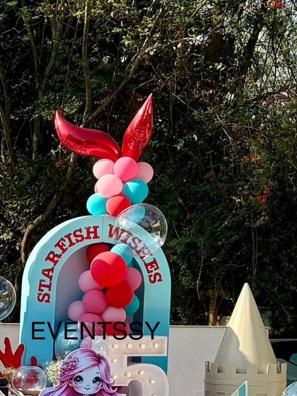 A close-up of the balloon arch from the mermaid party, featuring a red mermaid tail balloon. The arch frames the "Starfish Wishes" sign, adding to the underwater fantasy theme.