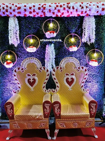 An elegant and simple stage for an engagement ceremony. This setup features two golden thrones against a green backdrop with hanging floral hoops, creating a beautiful focal point for the couple.