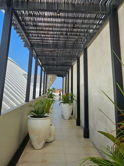 A beautifully designed corridor with a slatted roof and large white planters. We are always noticing great design details on our travels.
