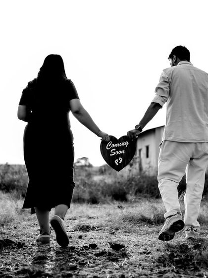A black and white shot of the couple walking away, holding a "Coming Soon" sign between them. It’s a perfect metaphor for walking into their future together.