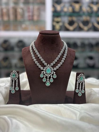 A double-layered AD necklace set with a central pendant. This versatile design comes in multiple colors including pink, white, emerald, and sapphire blue, making it a great addition to your inventory.