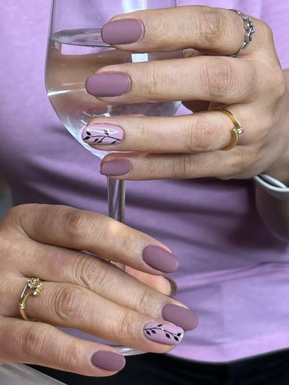 Classic matte nails in a beautiful dusty mauve. The look is elevated with two accent nails featuring a simple, hand-painted black leaf design.