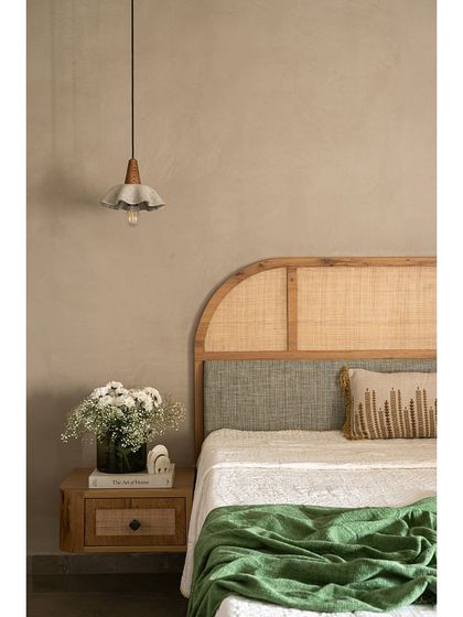 A close-up of the master bedroom's bedside. The headboard combines a cane panel with a textured fabric section. A floating nightstand with a cane drawer front continues the natural, earthy theme.