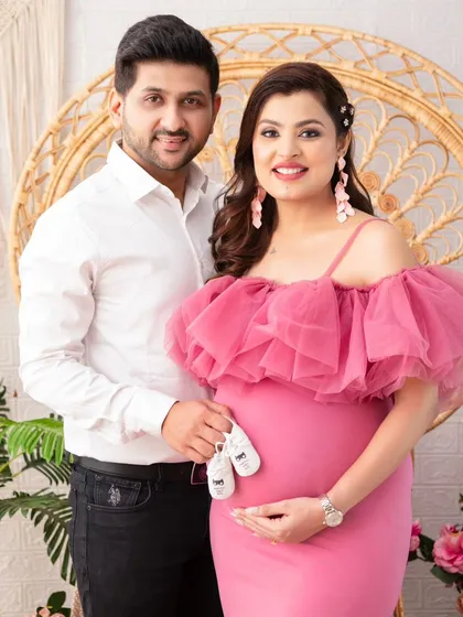 A classic couple's portrait. Standing together, they hold a pair of baby shoes over the bump, a simple and sweet announcement of their growing family.
