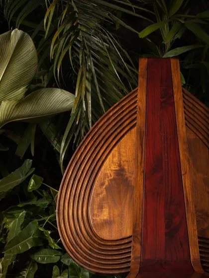 A detail shot of the Vismayam chair's backrest, where layers of wood are carved to ripple like the folds of a Theyyam costume. The central band of rich, red-toned wood is a direct nod to the fiery colors used in the art form.