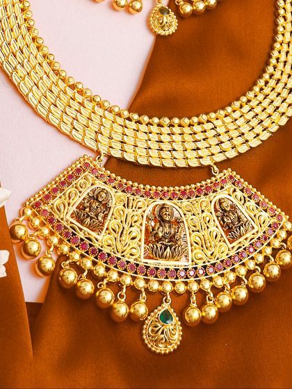 This necklace showcases detailed deity carvings within its pendant, a hallmark of our temple jewellery. The use of red stones and gold beads adds to its traditional appeal.