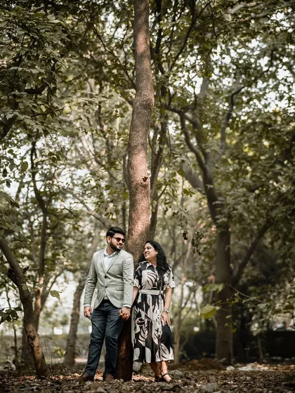 A wide shot of the couple in a serene forest setting. The tall trees create a beautiful, natural frame, emphasizing the feeling of being in their own private world.