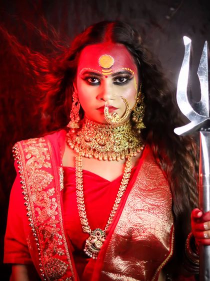 A powerful portrait of a goddess in red, holding a trishul, with dramatic makeup.