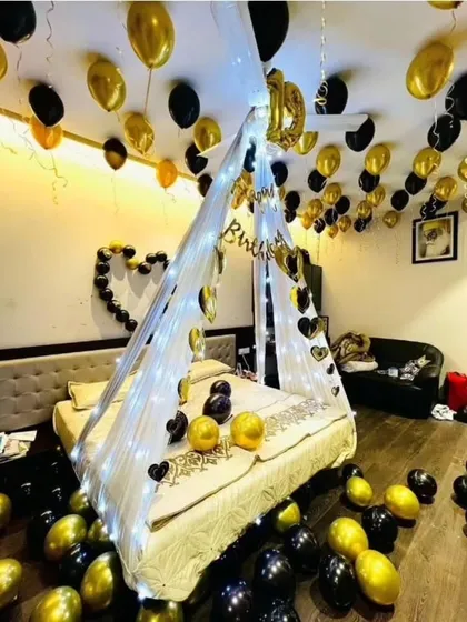 For a stylish and modern romantic look, I use black and gold balloons. This room decoration includes a canopy with fairy lights and balloons scattered on the floor and bed.