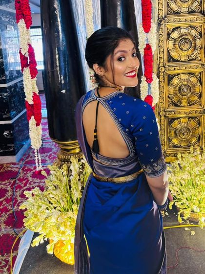 A client looking back with a smile, wearing a royal blue saree and a matching blouse with a keyhole back and simple embroidery.
