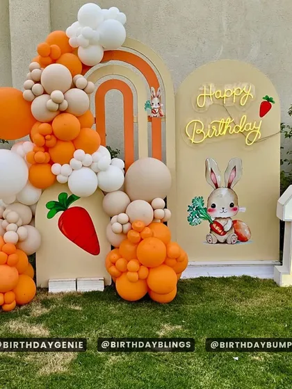 A cute bunny-themed birthday party, perfect for a spring celebration or a first birthday. The orange, cream, and white balloons complement the outdoor setting.