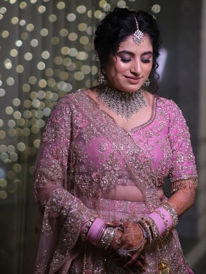 A moment of quiet grace. The bride looks down, showcasing her elaborate jewelry and the soft elegance of her pink wedding lehenga.