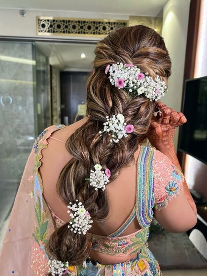 A voluminous pull-through braid with highlights, decorated with baby's breath and small pink flowers for a dreamy Mehandi look.