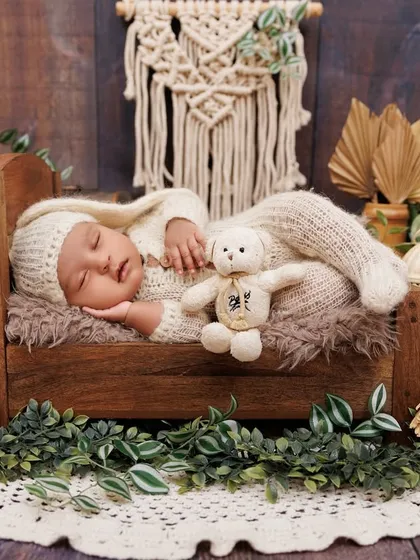 A full view of a sleeping newborn in a rustic wooden bed, surrounded by greenery and boho-chic decor.