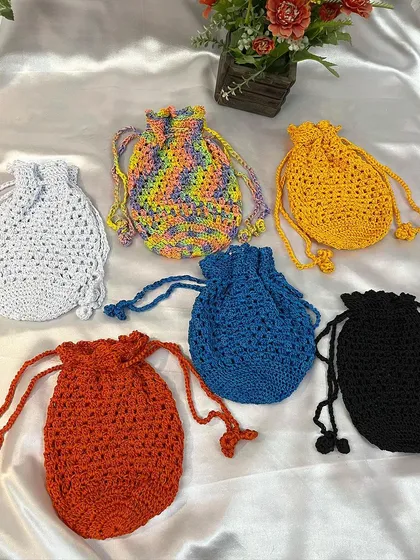 A vibrant collection of my handmade crochet potli bags. These drawstring pouches come in many colors, including solid white, blue, black, red, yellow, and a fun rainbow yarn, making them perfect for any occasion.